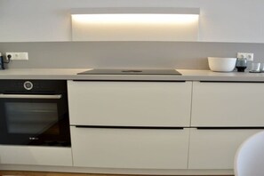 A modern kitchen with a built-in oven, a countertop with a bowl and a kettle, and a wall-mounted light fixture. - Holiday apartment with 1 bedroom (Friedrichshafen)