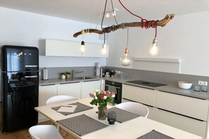 A modern kitchen with a black refrigerator, white cabinets, and a dining table with placemats. - Holiday apartment with 1 bedroom (Friedrichshafen)