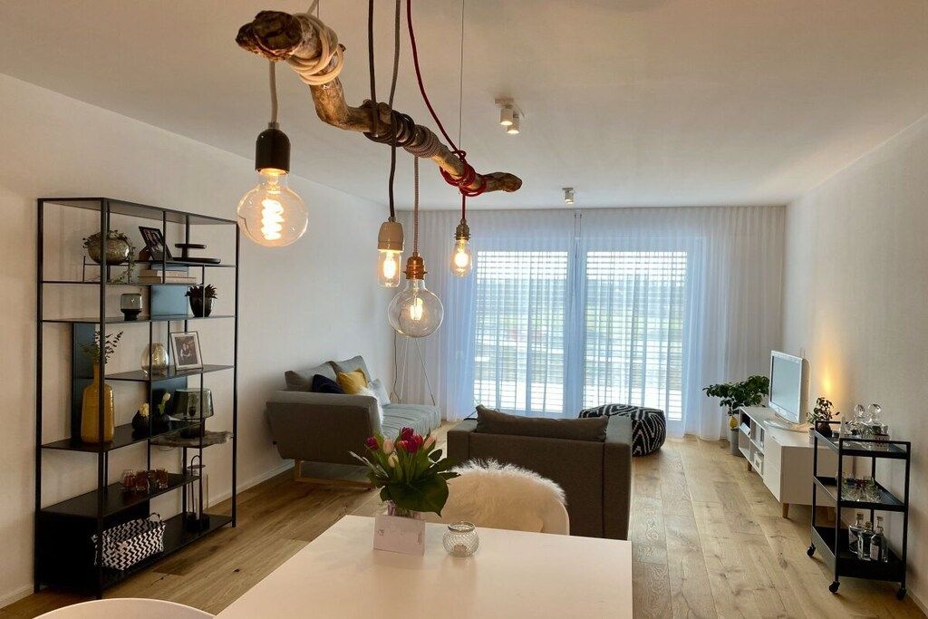 A modern living room with a white sofa, a coffee table with a vase of flowers, and a bookshelf.