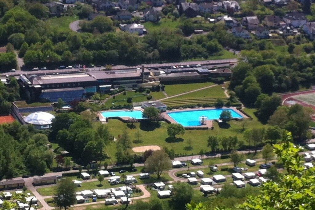 Eine Vogelperspektive auf ein Wohngebiet mit Schwimmbad, einem großen Gebäude mit Kuppel und einem Parkplatz mit Wohnmobilen.