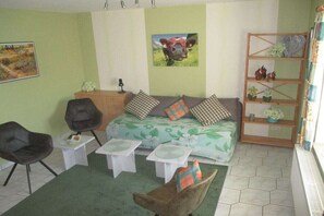 Ein Wohnzimmer mit einer Couch, zwei Sesseln, einem kleinen Tisch und einem Bücherregal.