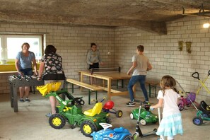 A room with a brick wall, a wooden table, and children's toys including toy cars and a scooter. - Holiday apartment with 3 bedrooms (Marsberg)
