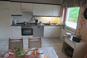 Cocina compacta con gabinetes blancos, estufa, pileta y comedor con mesa para dos.