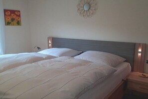 Ein Doppelbett mit grauem Kopfteil, zwei Nachttische und eine Wandleuchte.