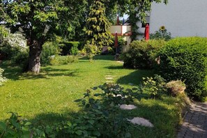 Ein Garten mit einem gepflasterten Weg, einem Baum und einem Gebäude mit einem roten Sonnenschirm.