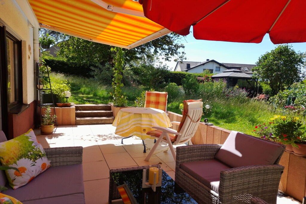 An outdoor patio with wicker furniture, a striped umbrella, and potted plants.