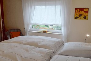 Une chambre à coucher avec un lit, une fenêtre ornée de rideaux légers et un tableau accroché au mur.