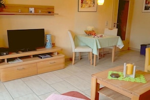 A cozy living room with a television, a wooden cabinet, a dining table with chairs, and a small table with candles. - Holiday apartment Sunflower with sauna and garden (Daun)