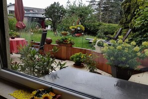 Blick durch ein Fenster auf einen Patio mit Tisch, Stühlen und Topfpflanzen.