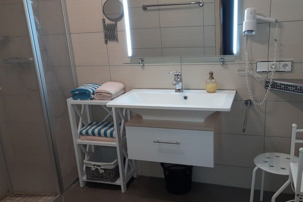 Un baño con lavamanos blanco, un espejo, toallero y secador de pelo.