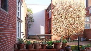 Een bakstenen gebouw met een klein terras, een houten tafel en diverse potplanten.