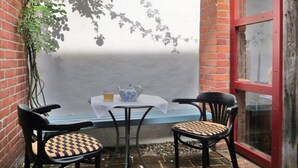 Een klein terras met een tafel en twee stoelen, een plant in pot en een raam met rode omlijsting.