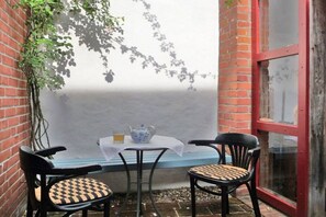 A small outdoor seating area with a table and two chairs, a potted plant, and a red-framed window. - Holiday apartment in Tangermünde with Wi-Fi (Tangermünde)