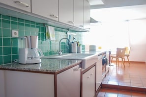 Een keuken met een koffiezetapparaat, een spoelbak en een stoel.