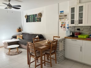 Ett kompakt bostadsutrymme med matplats, litet kök och en takfläkt.