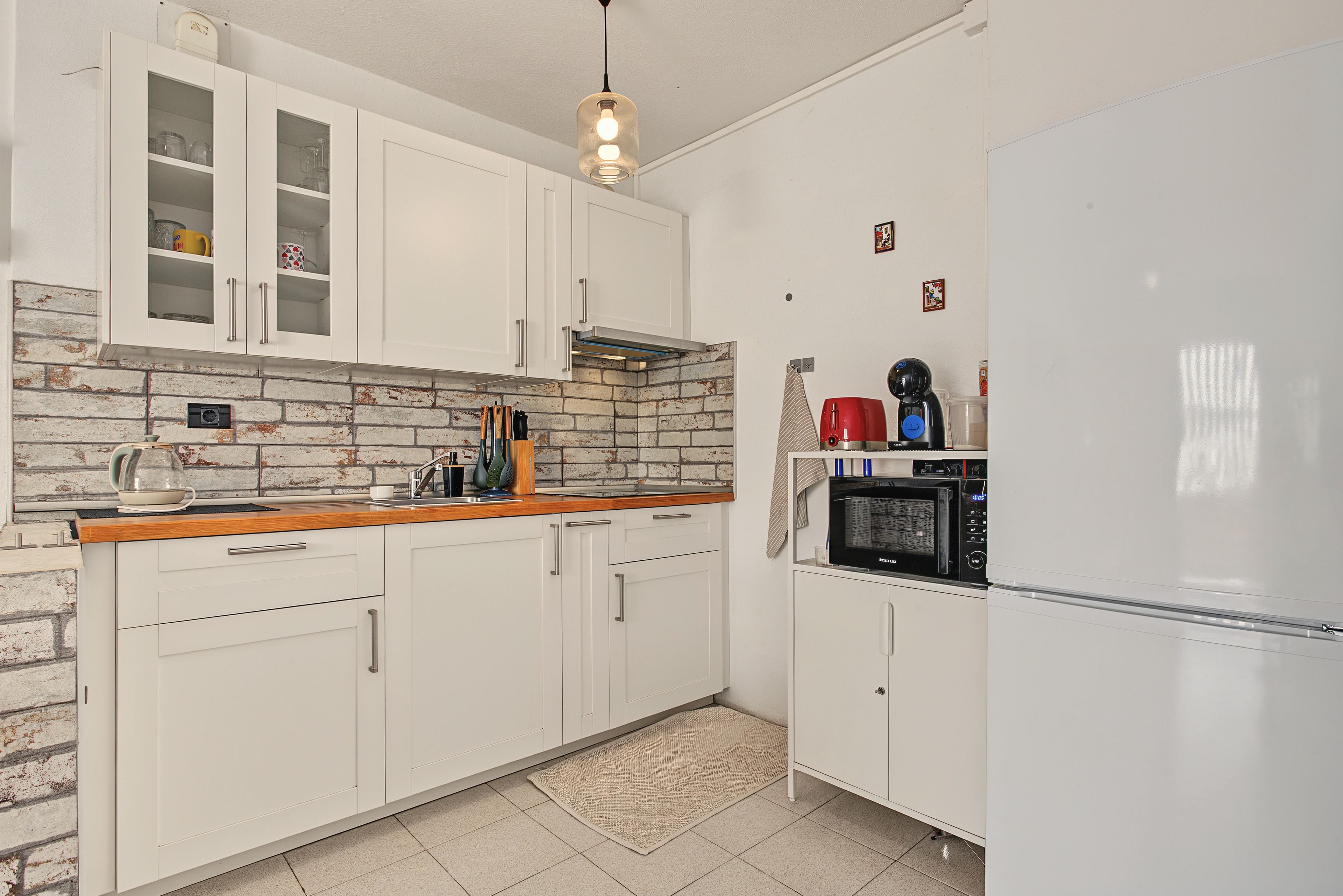 A kitchen with white cabinets, a brick backsplash, a wooden countertop, and a stainless steel range hood.