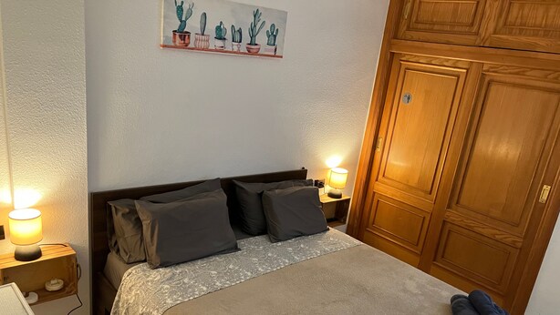 A neatly made bed with pillows, a bedside lamp, and a wall-mounted cactus decoration. - Holiday Apartment 'Casa Cactus Tenerife' with Pool, Teide Views, and Air Conditioning (Arona)
