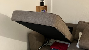 A sofa with an integrated storage compartment, a remote control on a small wooden stand, and a lamp on the stand. - Holiday Apartment 'Casa Cactus Tenerife' with Pool, Teide Views, and Air Conditioning (Arona)