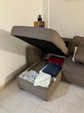 En soffa med ett inbyggt förvaringsutrymme, en fjärrkontroll på ett litet träställ och en lampa på stället.