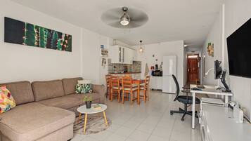 A modern living room with a sofa, a dining table, and a kitchen in the background.