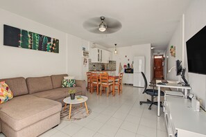 A modern living room with a sofa, a dining table, and a kitchen in the background.