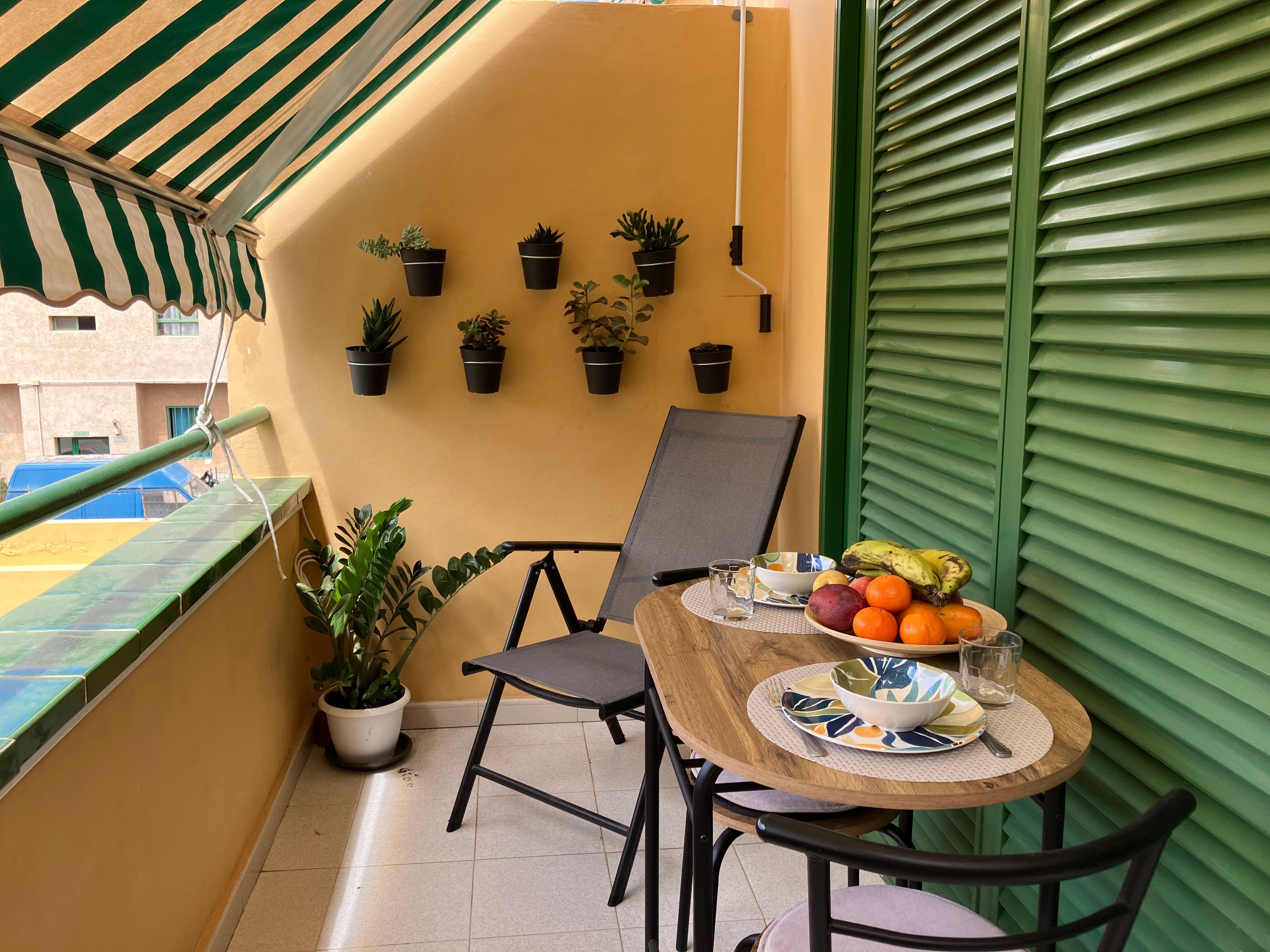 Un balcon avec une table dressée pour deux personnes, des plantes en pot et une vue sur la rue.