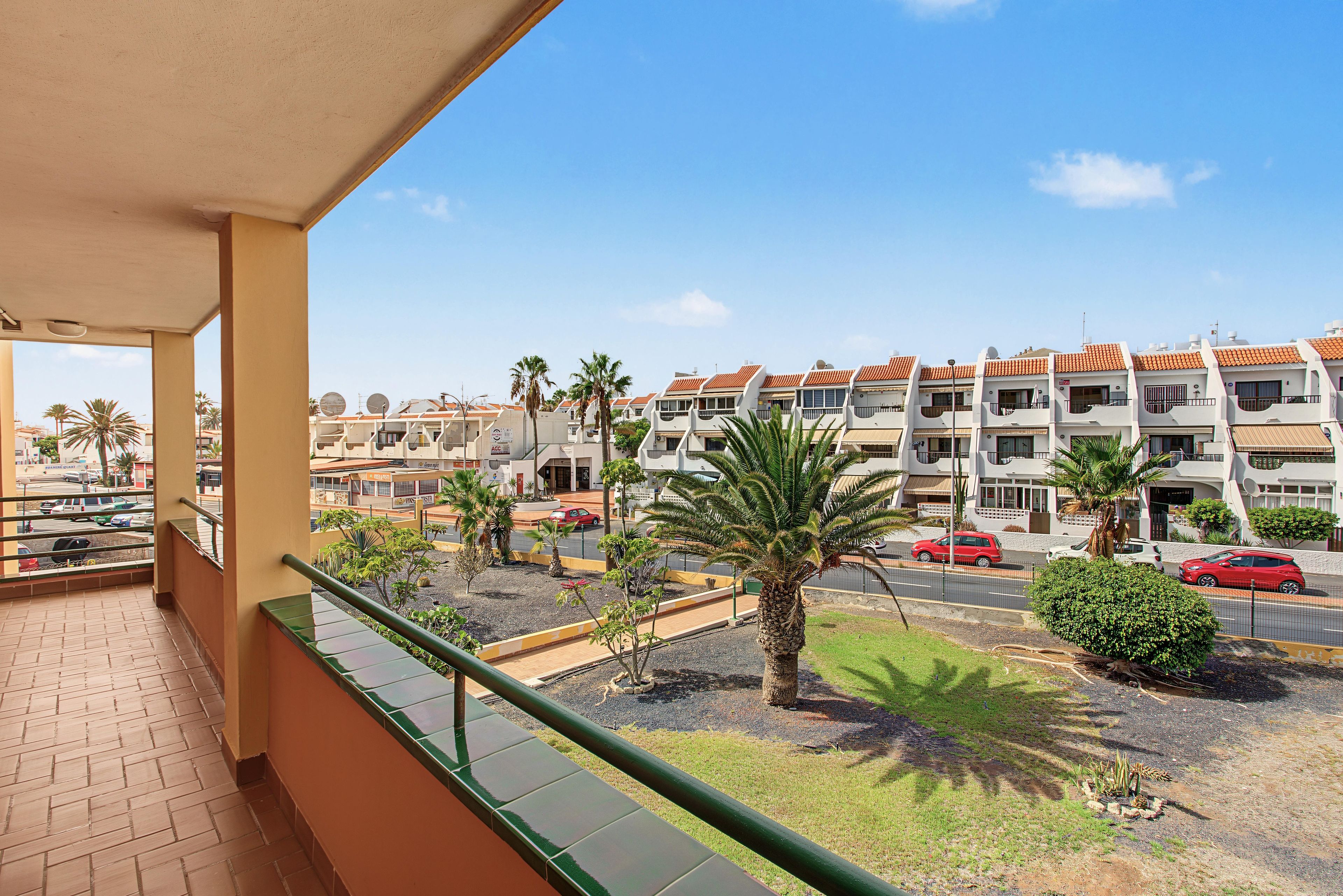 A balcony with a view of a residential area, including a row of houses with orange roofs and a street with cars.