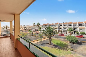 A balcony with a view of a residential area, including a row of houses with orange roofs and a street with cars.
