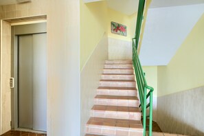 A staircase with a green handrail leading to a landing, a door on the left, and a wall with a floral painting.