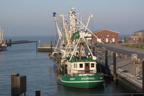 A green fishing boat docked at a pier with a building in the background. - Holiday apartment with 1 bedroom (Dornumersiel)