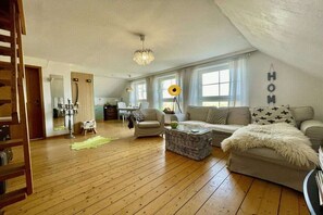 A spacious living room with a wooden floor, a sofa set, a coffee table, and a chandelier. - Holiday apartment with 1 bedroom (Dornumersiel)