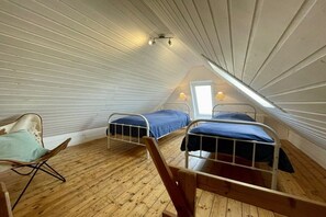 A small attic bedroom with two metal bunk beds, a wooden chair, and a sloped ceiling with wooden beams. - Holiday apartment with 1 bedroom (Dornumersiel)