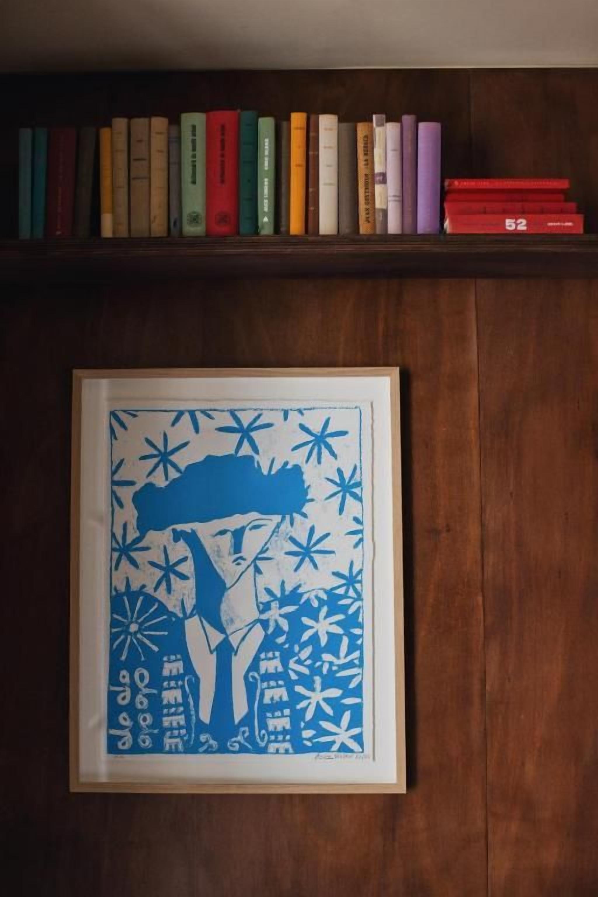 Una obra de arte en un marco sobre la pared, una estantería con libros y un panel de madera.
