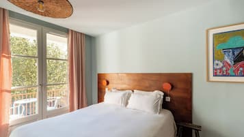 A hotel room with a large bed, a wooden headboard, a painting on the wall, and a balcony with a view of trees.