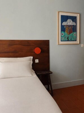 Ein Bett mit Holz-Kopfteil, ein kleiner Hocker und ein gerahmtes Kunstwerk an der Wand.