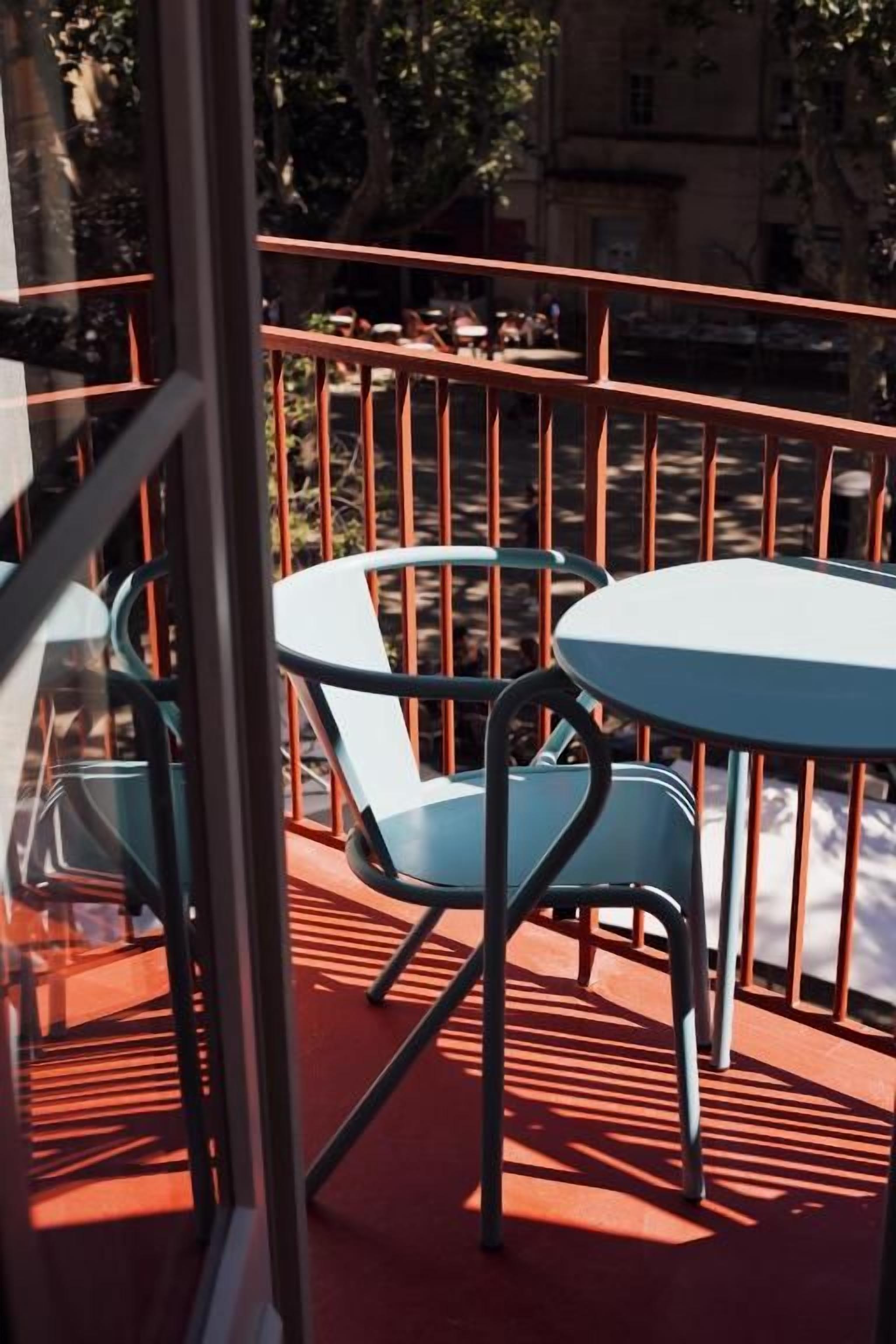 Una terraza con barandas metálicas, un separador de vidrio y dos mesas redondas con sillas.