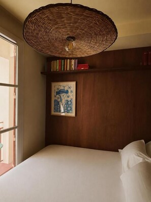Ein Schlafzimmer mit einem Bett, einer gewobenen Deckenleuchte, einem gerahmten Kunstwerk und einem Bücherregal mit Büchern.