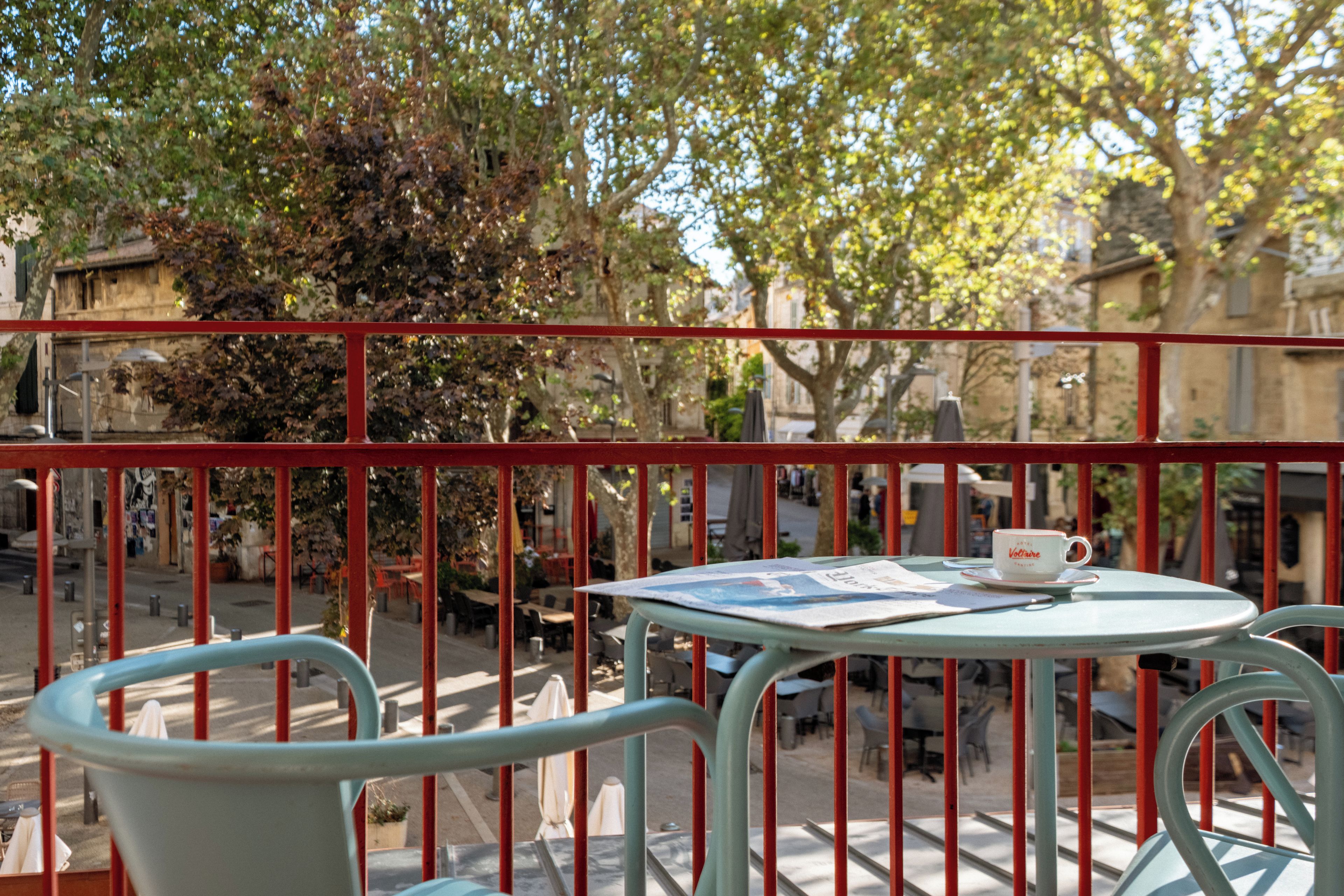 Un balcon avec une table et des chaises, un journal et une tasse.