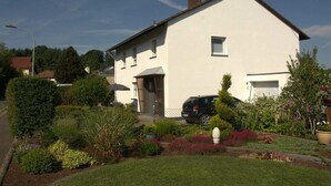 A two-story house with a car parked in the driveway, surrounded by a well-maintained garden with various plants and a lawn. - Holiday home in Eifel with 4 bedrooms (Dockweiler)