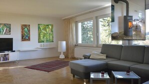 A modern living room with a sofa, a television, artwork on the wall, and a wood-burning stove. - Holiday home in Eifel with 4 bedrooms (Dockweiler)