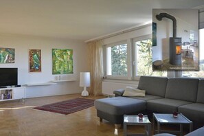 A modern living room with a sofa, a television, artwork on the wall, and a wood-burning stove. - Holiday home in Eifel with 4 bedrooms (Dockweiler)