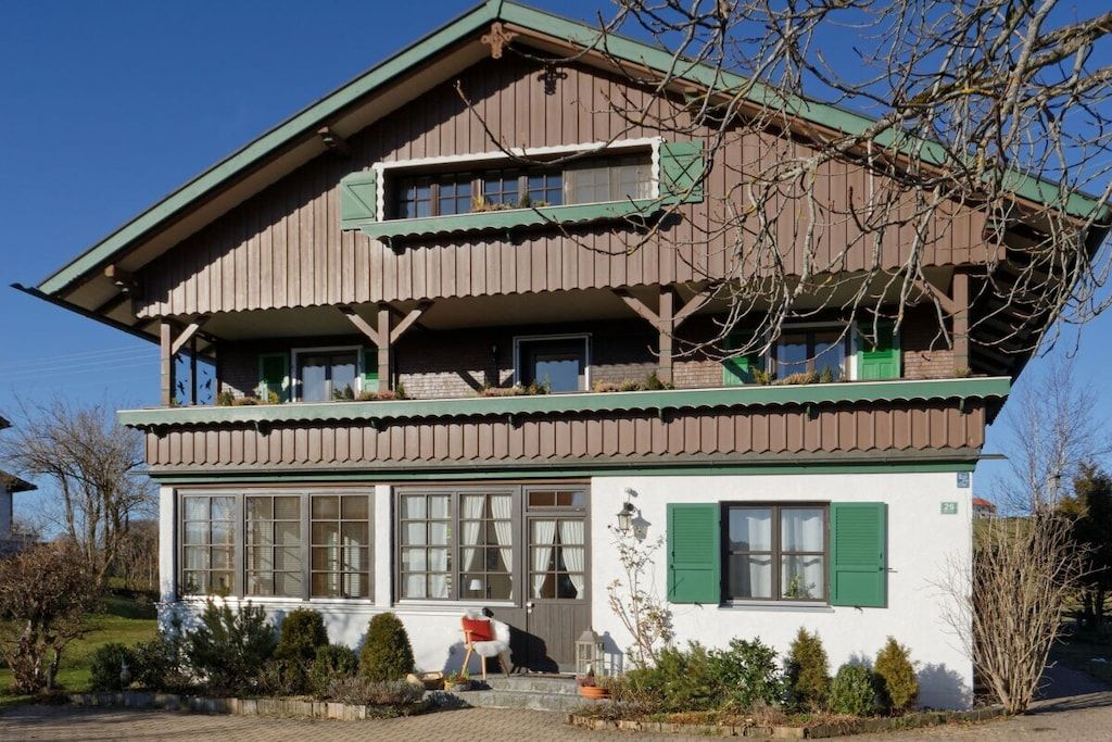 A two-story chalet with a balcony, large windows, and a well-maintained garden.