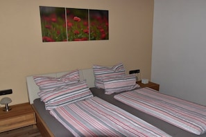 Un lit double avec une literie à rayures, une table de chevet avec une lampe et un tableau représentant des fleurs accroché au mur.