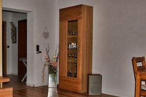 Ein Zimmer mit einem Holzkabinett, das Gläser, eine Blumenvase, einen Holzsessel und einen kleinen Lautsprecher enthält.