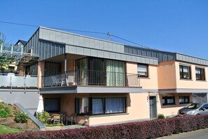 A two-story residential building with a balcony, a small outdoor seating area, and a car parked in the driveway. - Holiday apartment with 1 bedroom (Maring-Noviand)