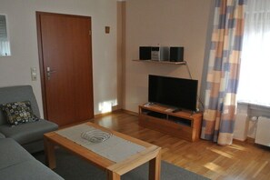 A living room with a sofa, a coffee table, a TV on a stand, and a door. - Holiday apartment with 1 bedroom (Maring-Noviand)