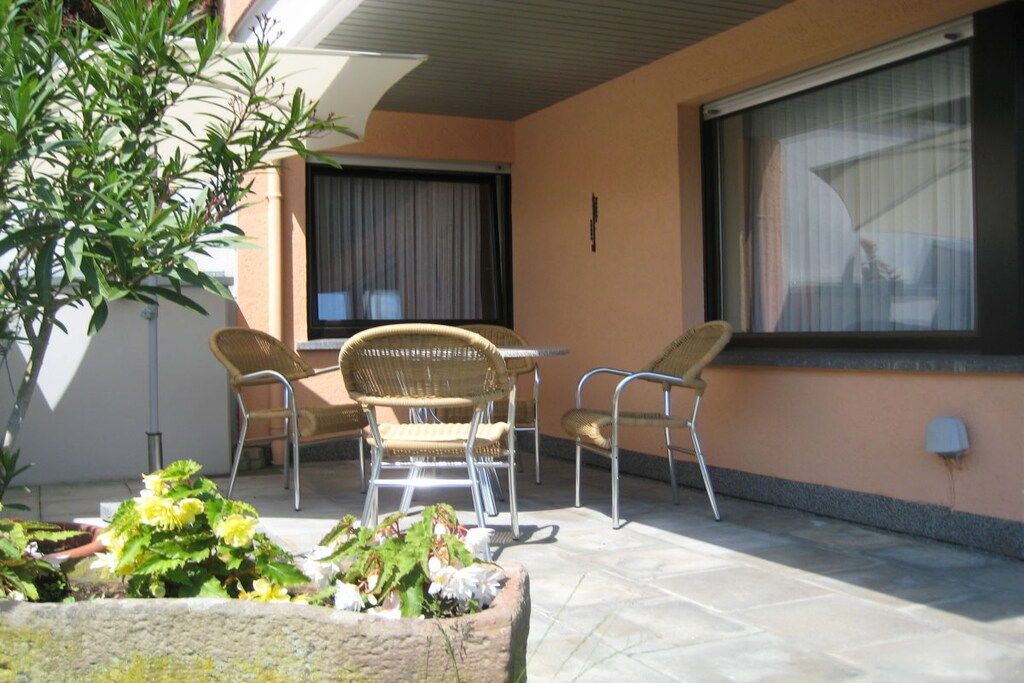 Un patio con una mesa, dos sillas, una planta en maceta y una ventana con persianas.