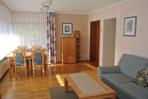 A living room with a sofa, a dining table with chairs, a wooden cabinet, and a window with curtains. - Holiday apartment with 1 bedroom (Maring-Noviand)