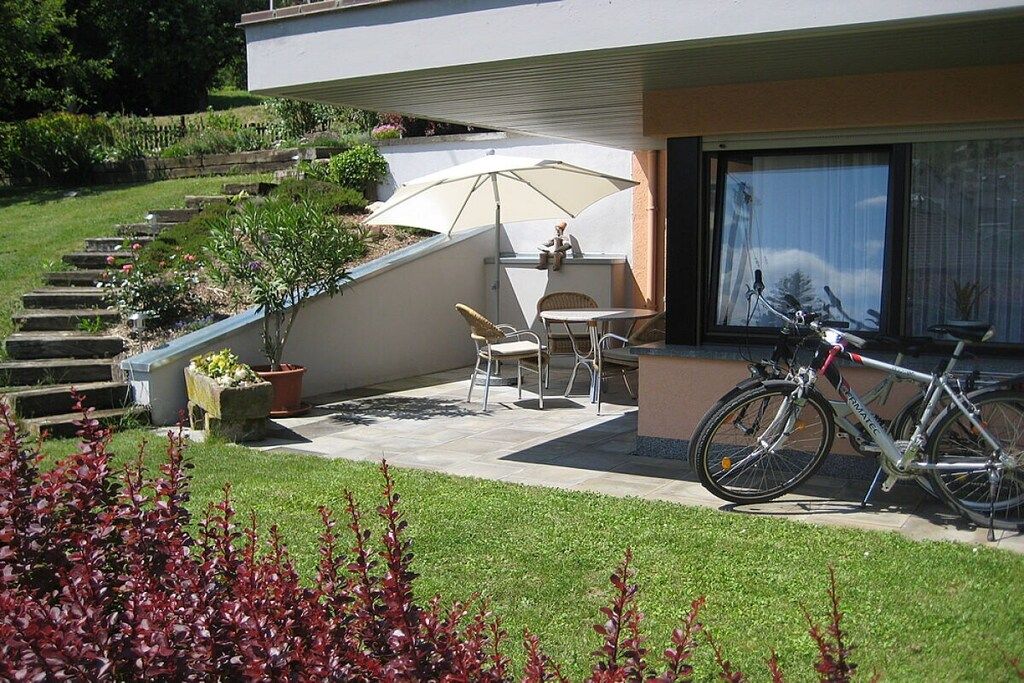 Eine Terrasse mit Tisch und Stühlen, ein Fahrrad und eine Treppe, die zu einem Gebäude führt.