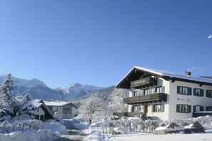 Ein Hotel mit Balkon, verschneiter Umgebung und Bergen im Hintergrund.